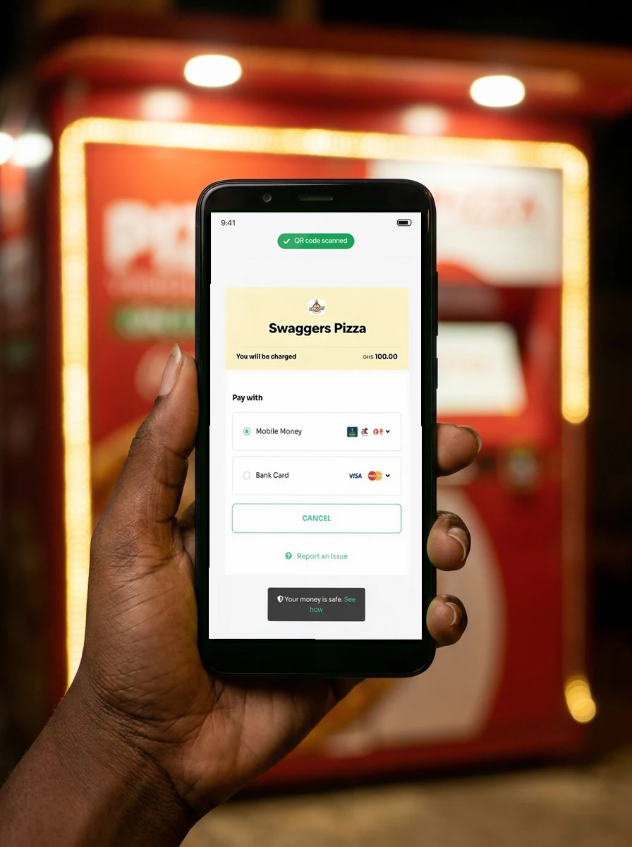 A hand holding a phone showing the Swaggers checkout after scanning the QR code: pay GHS 100 with Mobile Money or bank card